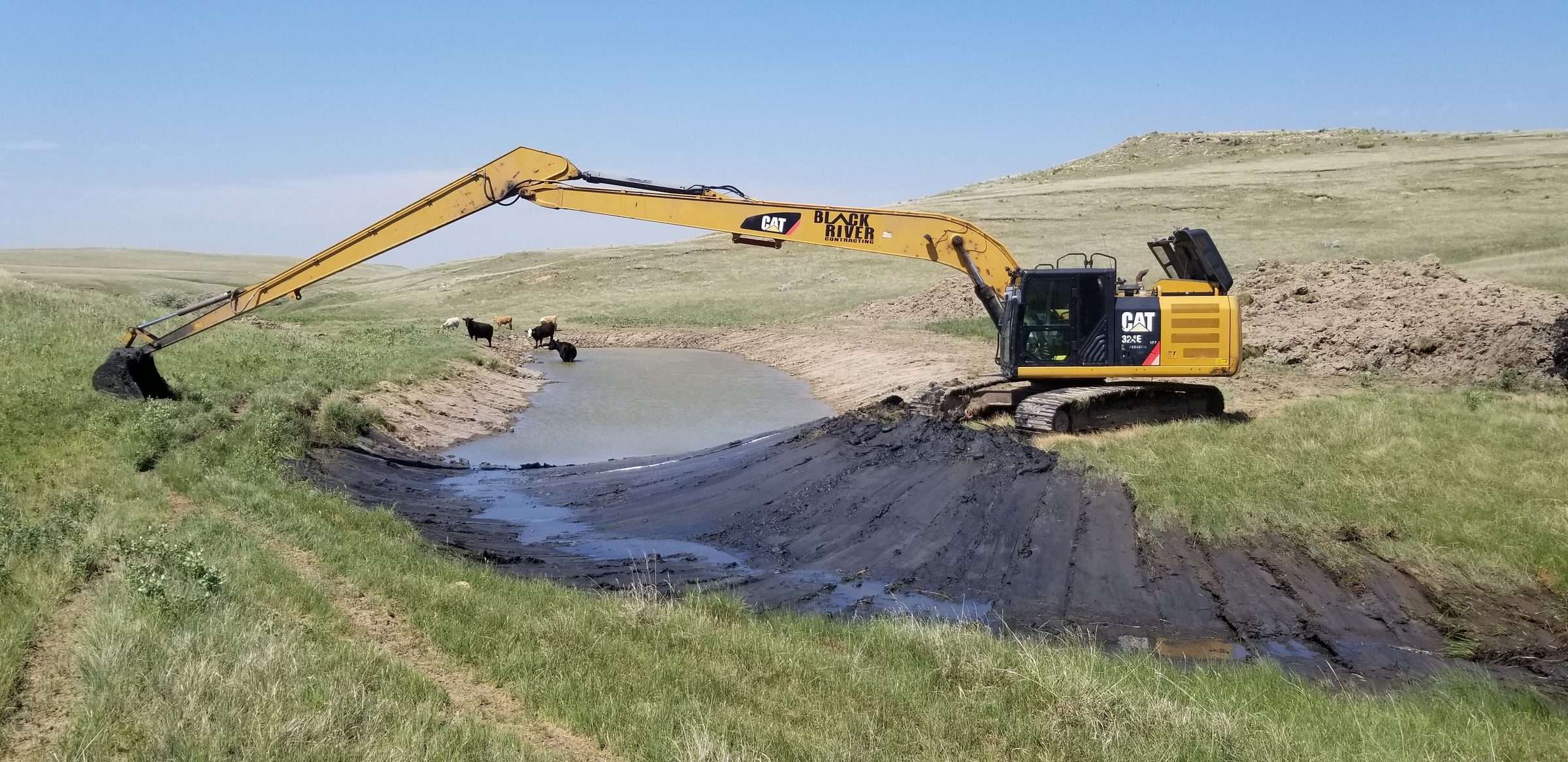 Long-reach excavator cleaning out a stock pond on a ranch