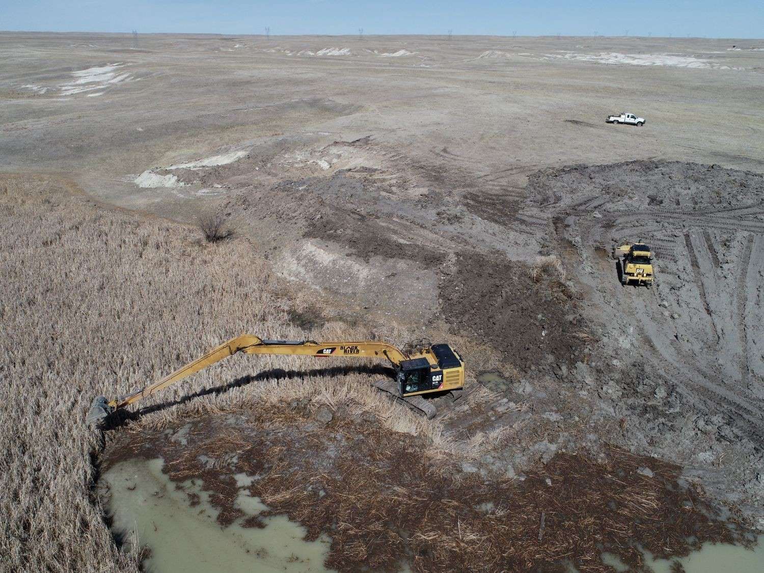 Aerial view of the Black River long-reach excavator clearing cattails and silt from a prairie pond