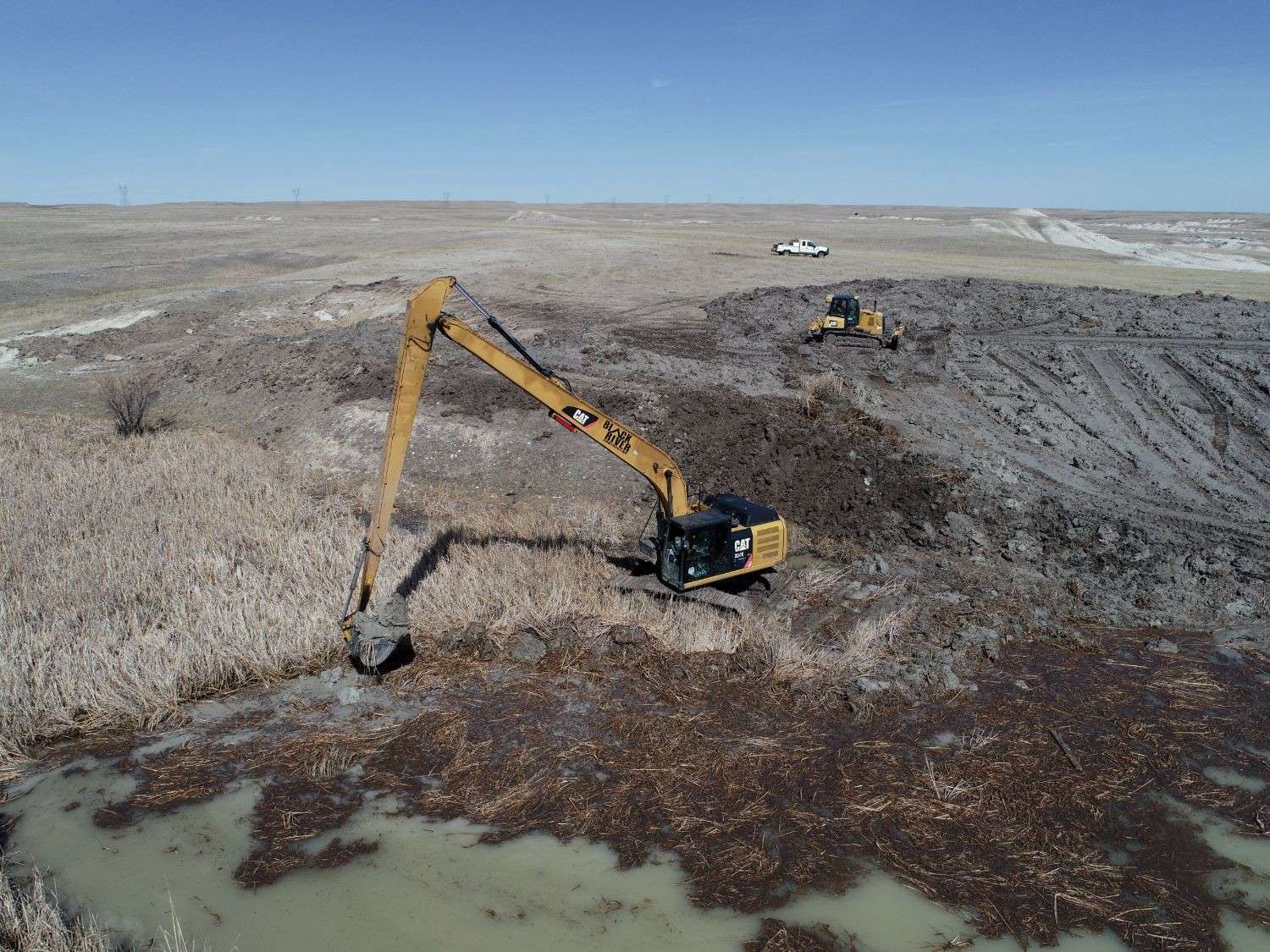 Aerial view of a Black River long-reach excavator cleaning out a prairie pond while a dozer spreads the spoil