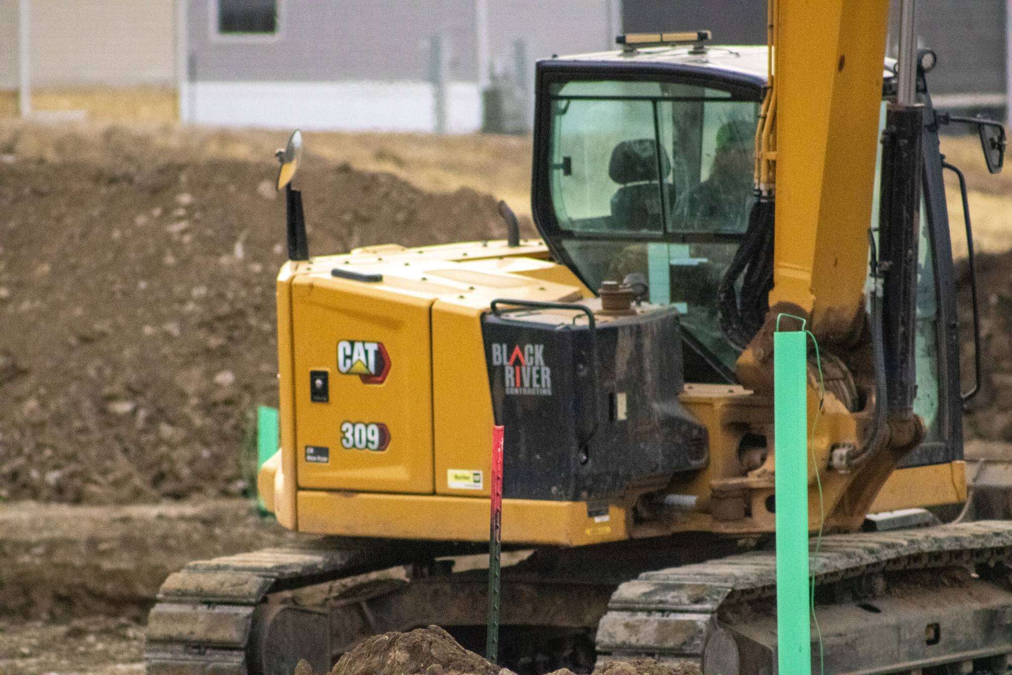 Black River Cat 309 excavator digging beside marker stakes on a subdivision job