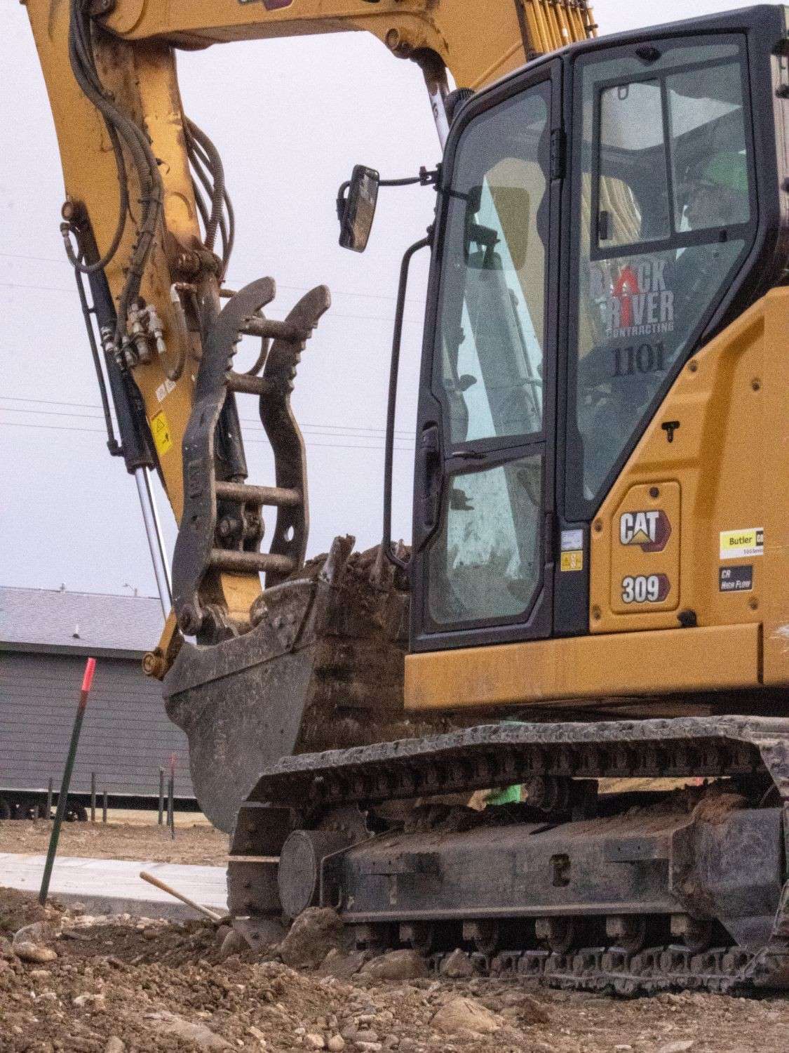 Black River Cat 309 excavator with a thumb attachment digging next to a new sidewalk